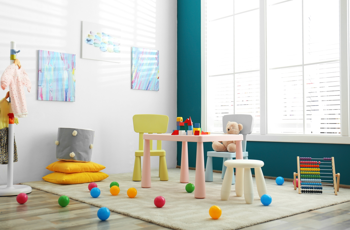 A bright children's playroom with colorful balls on a neutral area rug and stackable cushions arranged to support indoor active play for toddlers