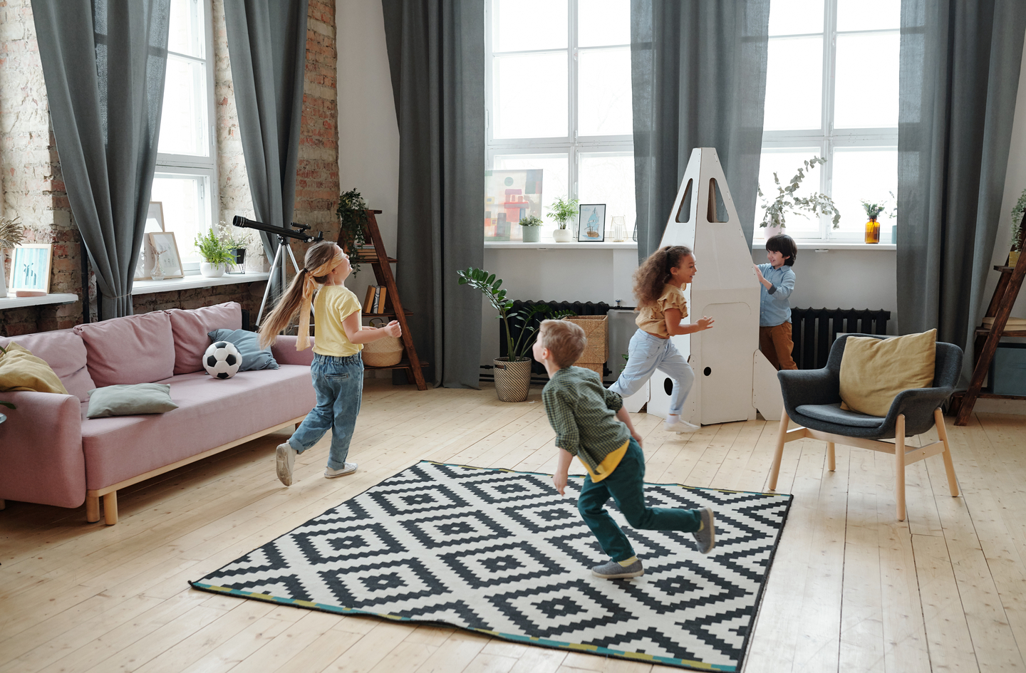Four children playing actively in a bright modern living room on a geometric rug - open floor space as the foundation of an indoor active-play zone