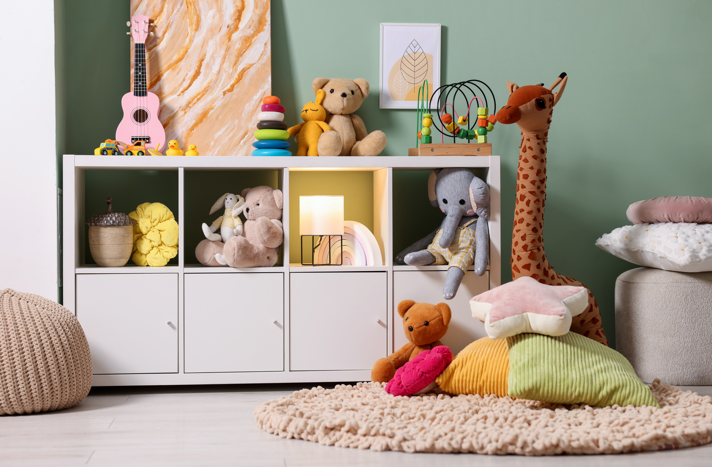 A white floor-to-ceiling shelving unit organized with toys, plush animals, and books stands against a sage green wall, demonstrating vertical storage that concentrates all inventory on the wall and leaves the floor clear