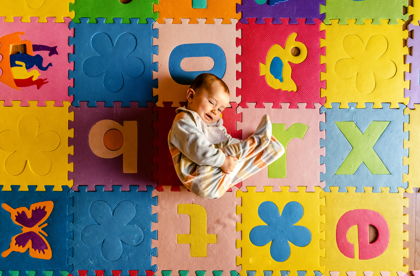 Baby lying on colorful interlocking foam baby play mat with alphabet letters and shapes