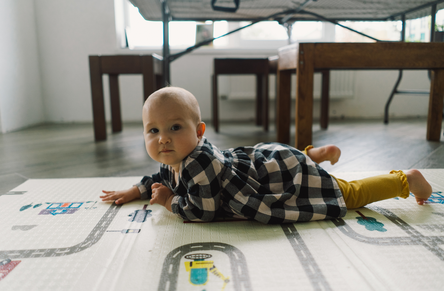 Baby lying on a non-toxic play mat with a road-patterned surface on the floor in a brightly lit room