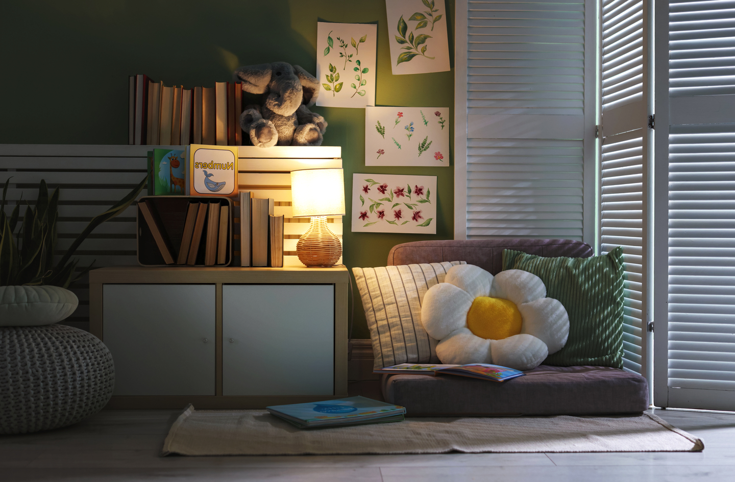 A cozy children's reading corner with soft seating, a lamp, and books displayed face-out on low shelves