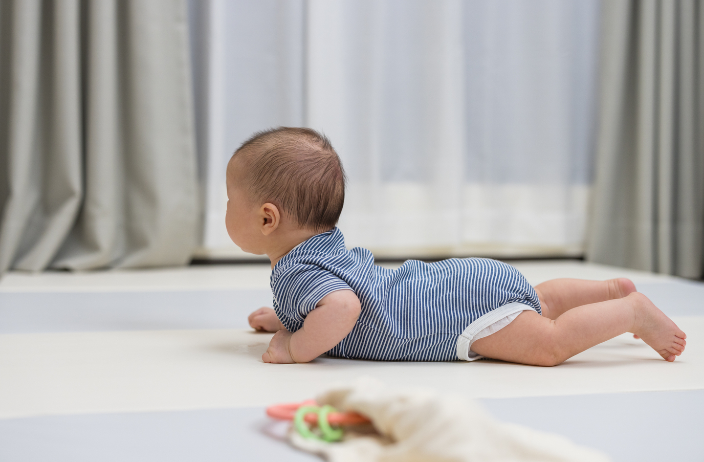 An infant lifts their head during tummy time on a play mat while looking toward a window