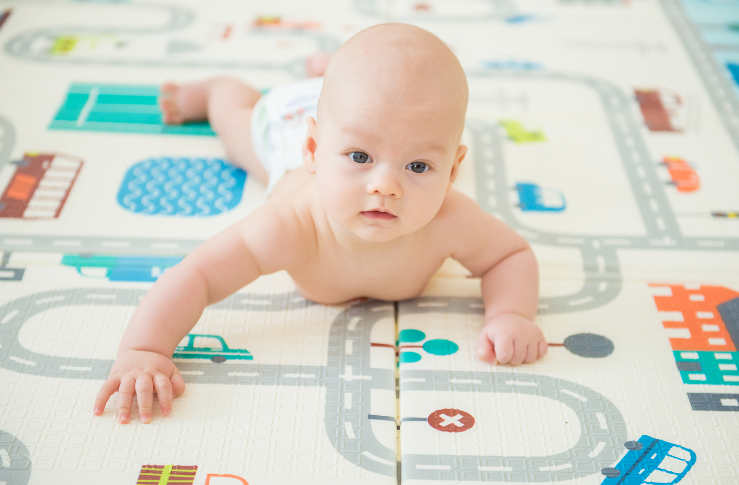 A newborn lying on the stomach on an infant activity mat lifting the head to look at the camera during tummy time