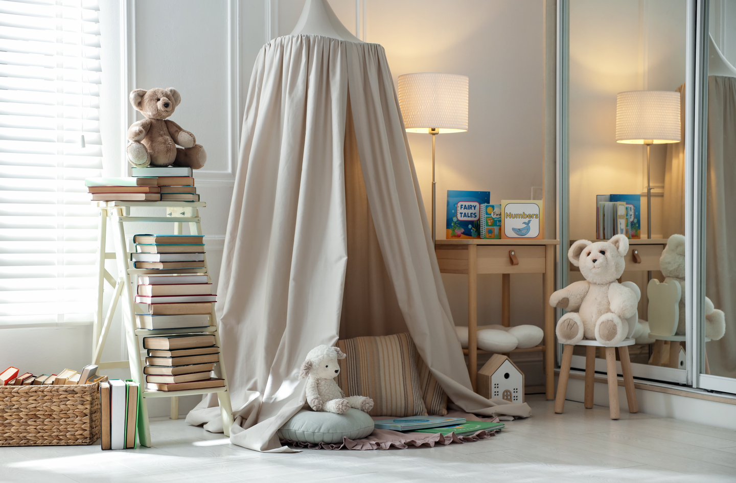 Kids reading nook with a soft fabric canopy over a round floor area, a ladder shelf of books and a small wooden table