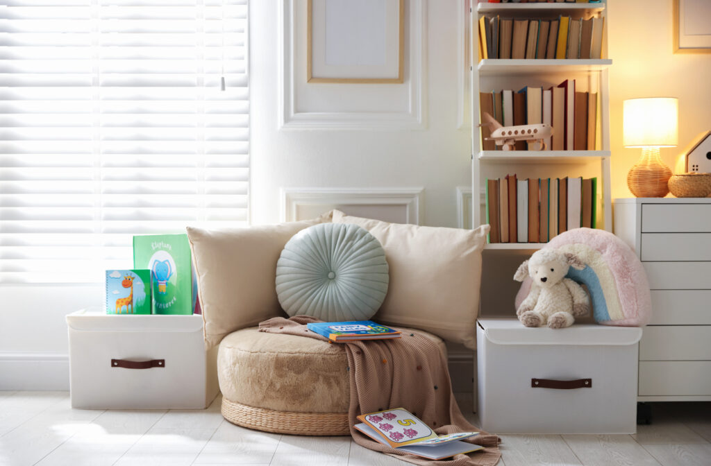 Kids reading nook with a round plush floor seat, cushions, white book bins and a low bookshelf