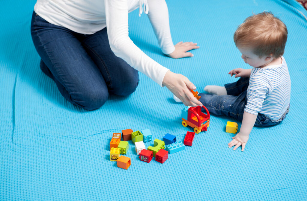 Playroom materials and surfaces in use: a parent and young child playing with building blocks on a blue foam play mat