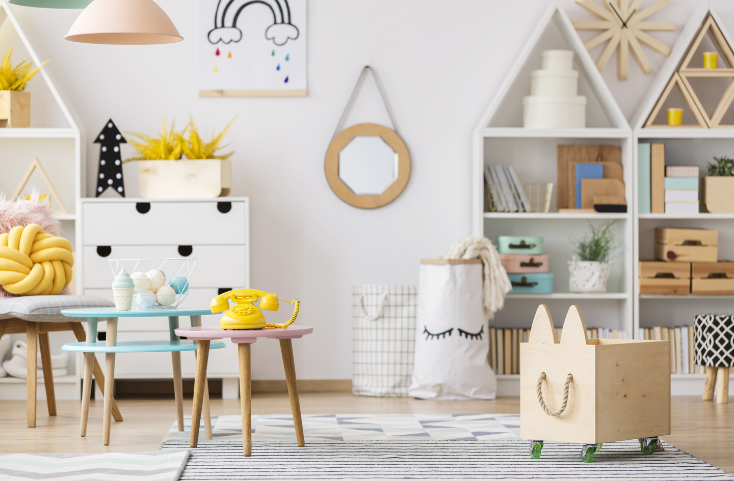 Small playroom storage with white house-shaped shelving, wooden toy bins, and small colorful tables